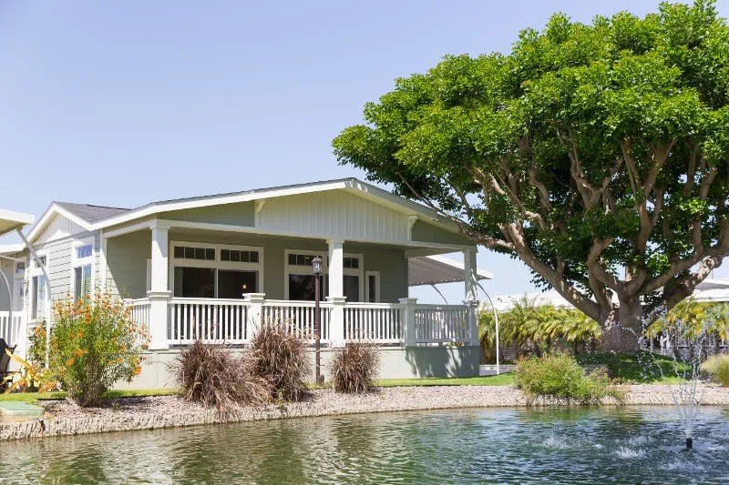 Manufactured home with a front porch beside a landscaped pond